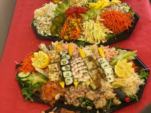 Rij schotels met huzarensalade, rauwkost, sushi, garnalen en vis op een rood tafelkleed